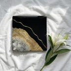 A square, black resin art piece with gold accents and a textured, gold and white section. A gold line runs diagonally across the black surface. The number "39" is visible. A white lily flower is in the image.