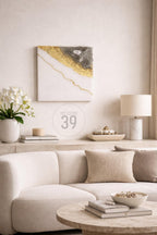 A modern living room scene featuring a white sofa, marble table, and decorative elements. A square wall art piece with gold and gray accents hangs above the sofa. The text "ART STUDIO 39" is visible.