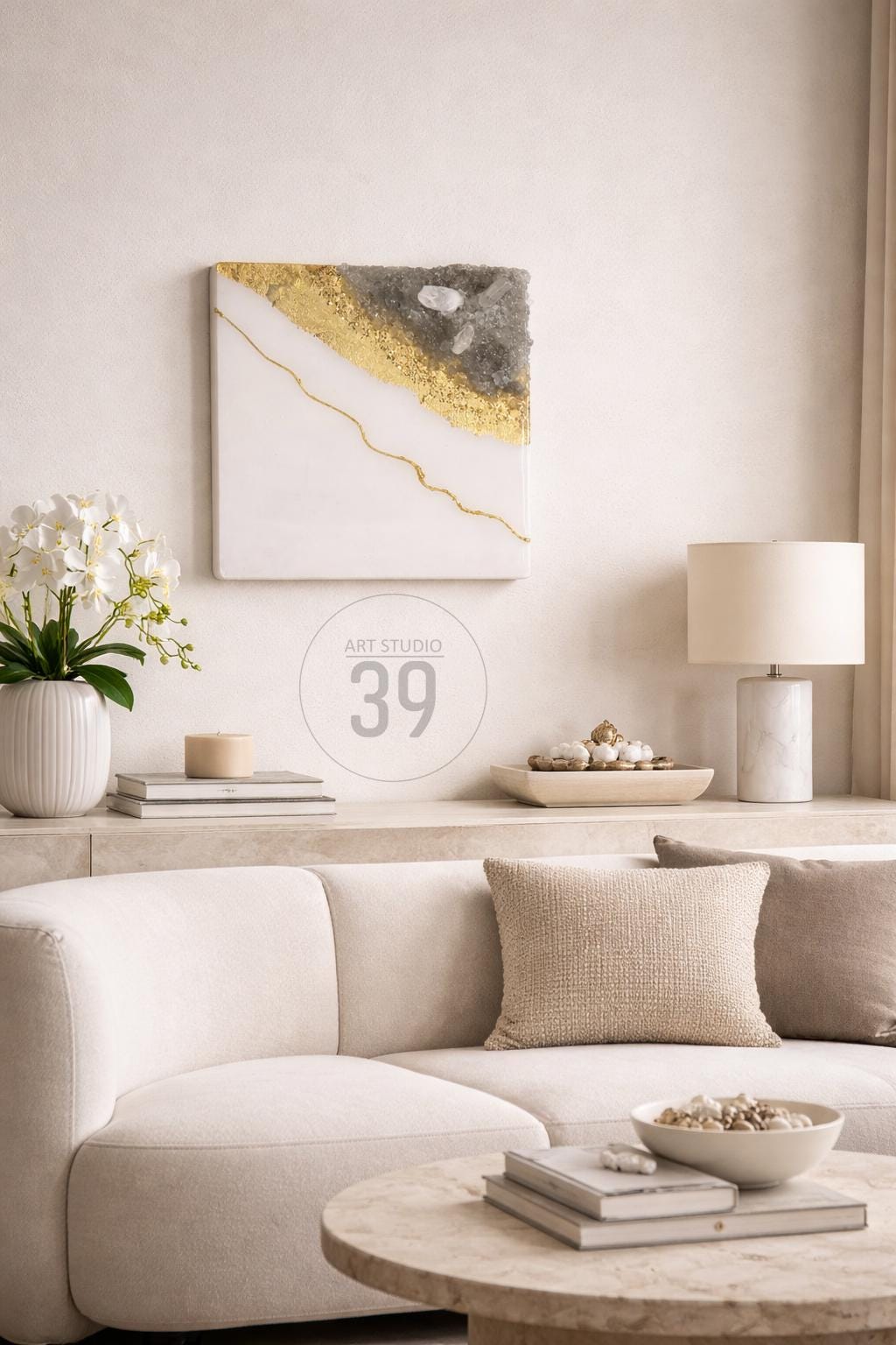 A modern living room scene featuring a white sofa, marble table, and decorative elements. A square wall art piece with gold and gray accents hangs above the sofa. The text "ART STUDIO 39" is visible.