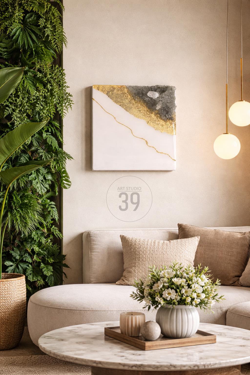A modern living room with a white sofa, decorative pillows, and a round coffee table. A square abstract art piece with gold and gray accents hangs on the wall. The image also features a vertical garden and pendant lights.