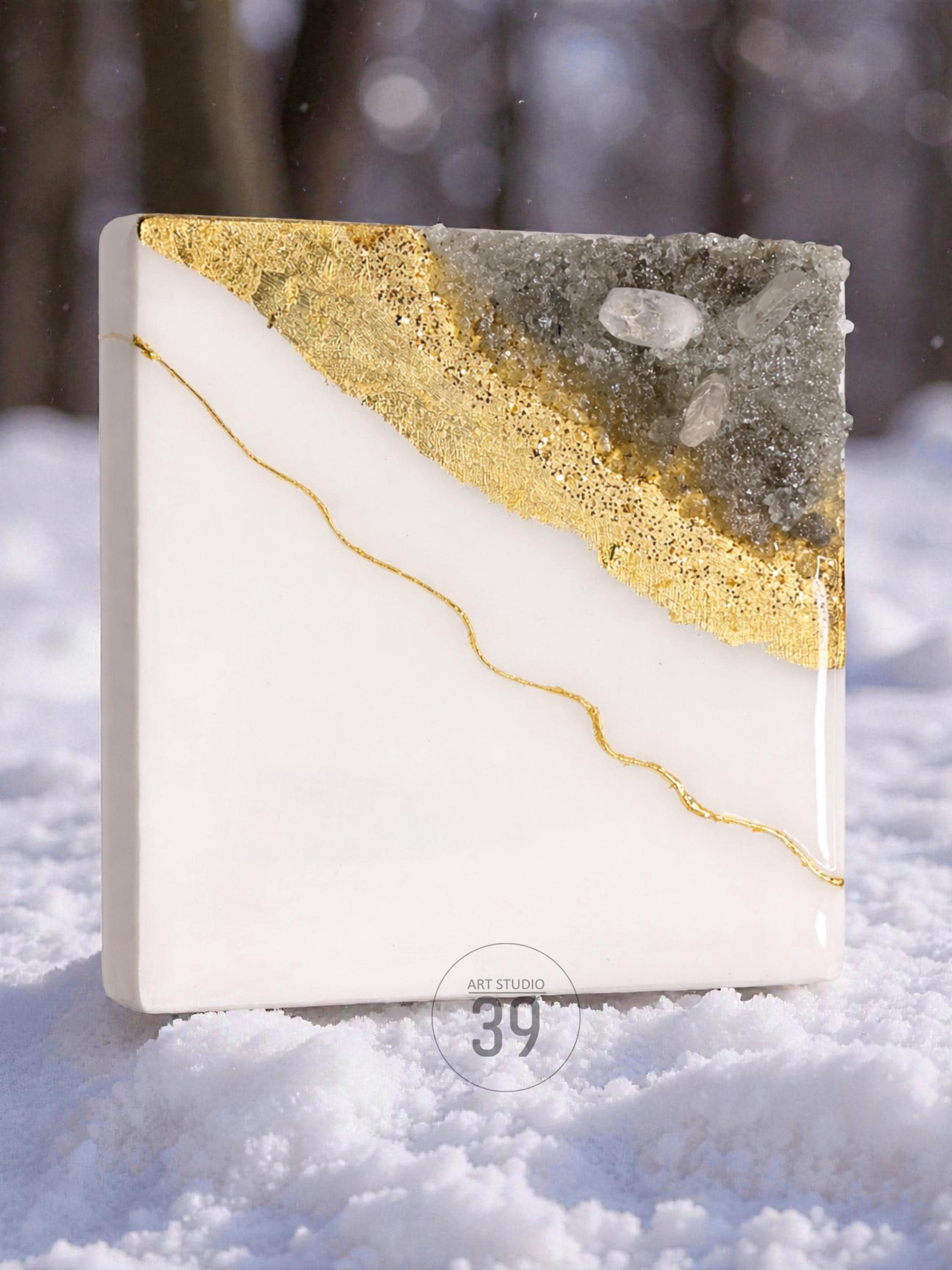 Square resin art piece with a white base, a diagonal section of gold leaf, and a gray, crystal-like section. A thin gold line curves across the white area. The text "ART STUDIO 39" is in a circle at the bottom.
