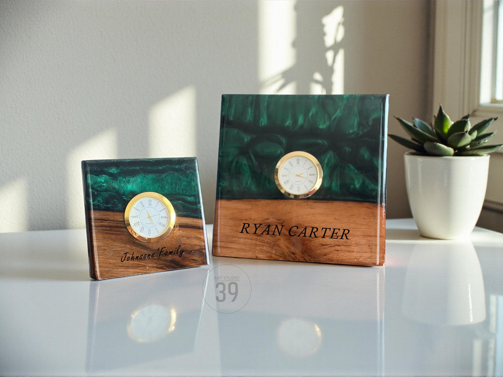 Two square wooden clocks with a gold-colored clock face. The top half of the clocks are dark green, and the bottom half is wood-toned. One clock reads "Johansen Family", and the other reads "Ryan Carter".