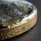 Close-up of a round object with a gold-colored textured edge. The top surface features a swirling design of black, white, and gold. The number "39" is etched into the gold edge.