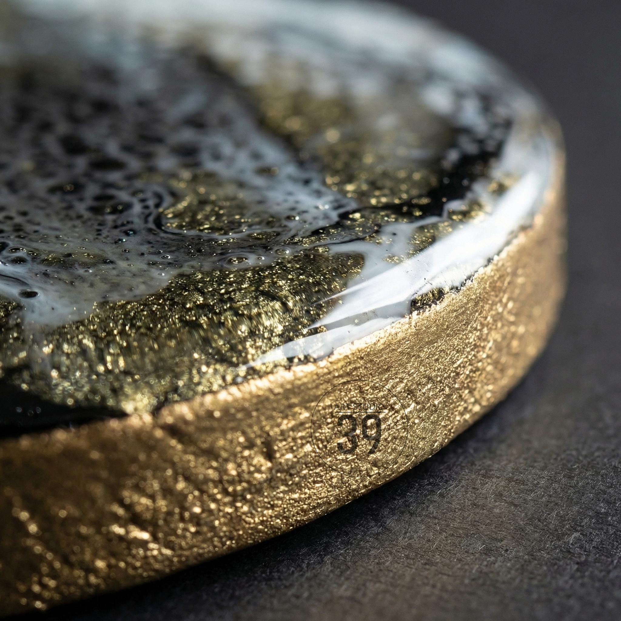Close-up of a round object with a gold-colored textured edge. The top surface features a swirling design of black, white, and gold. The number "39" is etched into the gold edge.