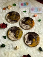 Four round coasters with abstract designs in shades of brown, gold, and white. The coasters are arranged on a textured white surface, with small decorative elements scattered around. The text "ART STUDIO 39" is visible.