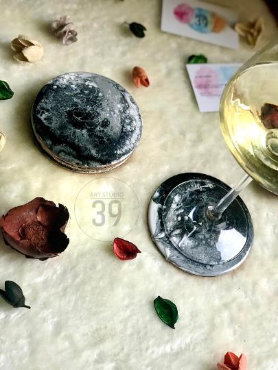 Two round coasters with a marbled black and white design. A wine glass sits on one coaster. The image also includes decorative leaves and flower petals. The coasters are part of a home decor set.