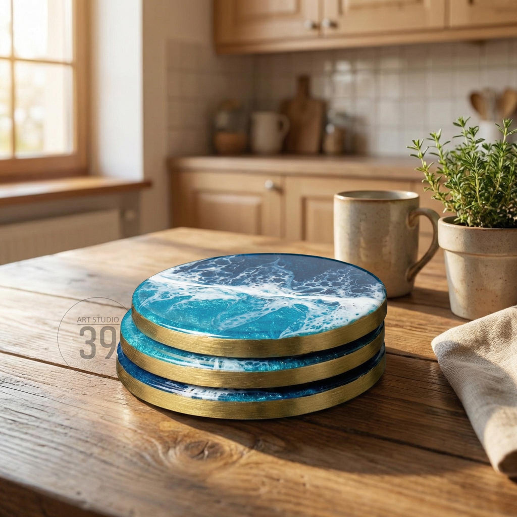 A stack of three round coasters with a blue and white ocean wave design. Each coaster has a gold-colored rim. The coasters are on a wooden table in a kitchen setting. The text "ART STUDIO 39" is visible.