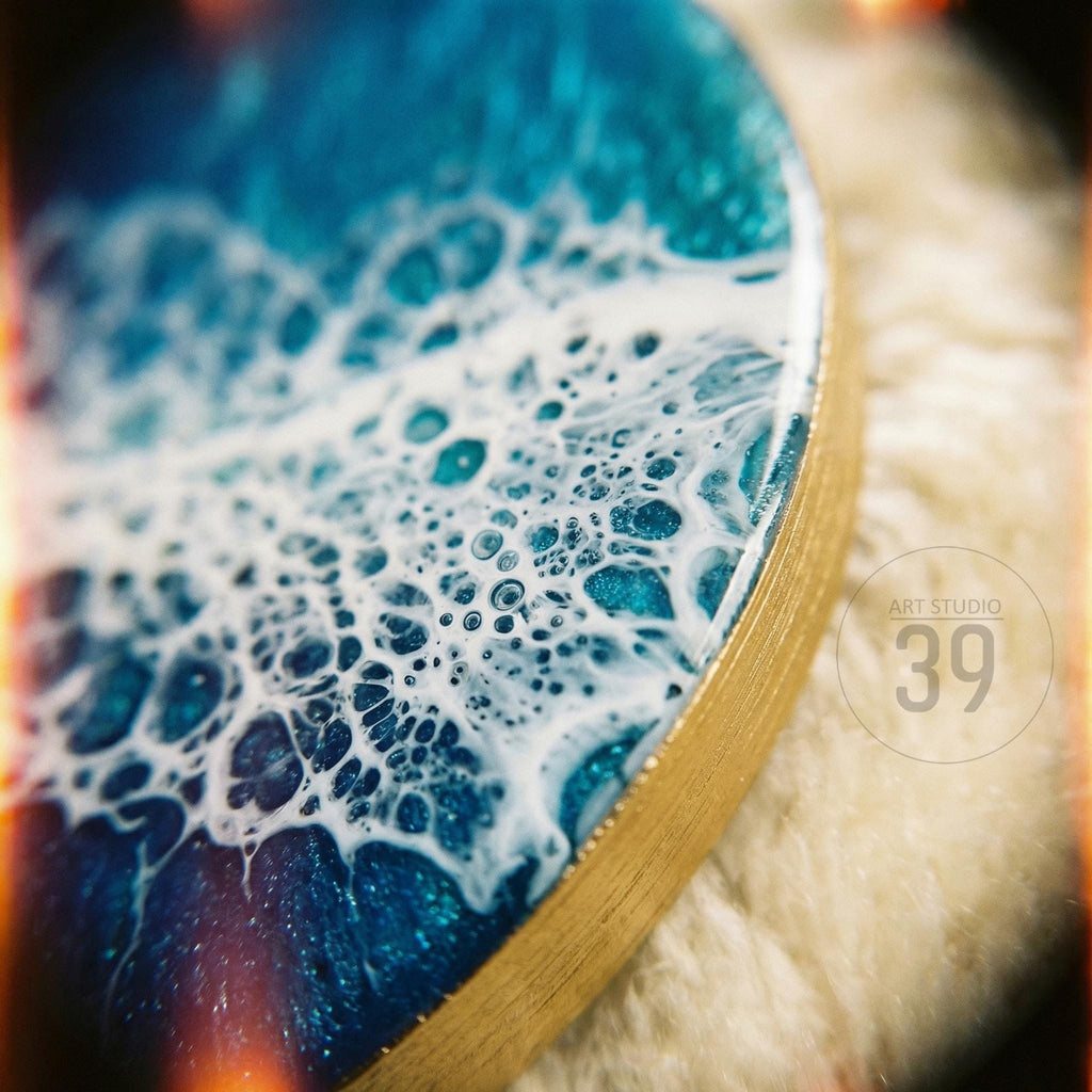 Circular resin art piece with a gold edge, featuring a blue and white ocean wave design. The artwork has a textured, bubbly appearance, with the text "ART STUDIO 39" in the corner.