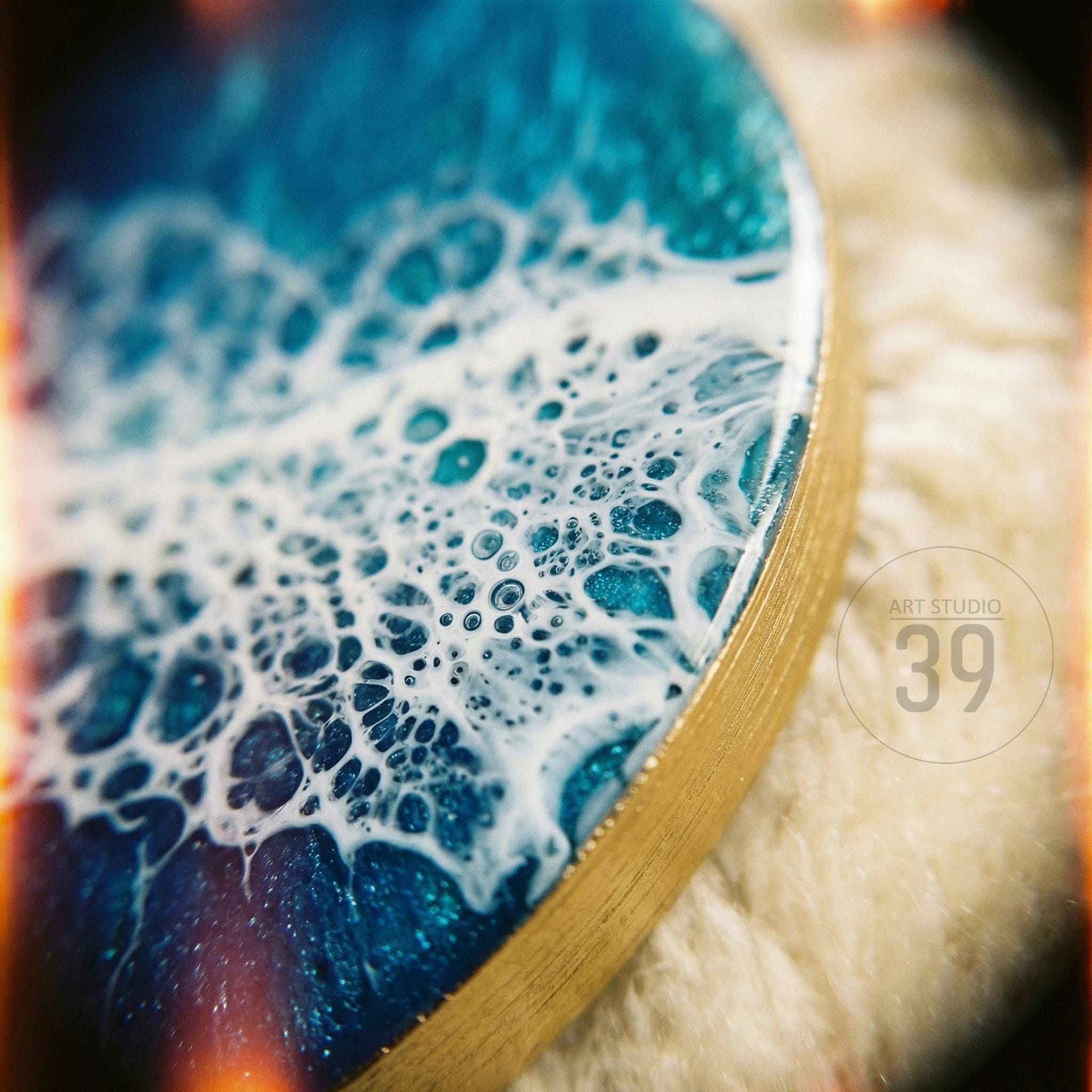 Circular resin art piece with a gold edge, featuring a blue and white ocean wave design. The artwork has a textured, bubbly appearance, with the text "ART STUDIO 39" in the corner.