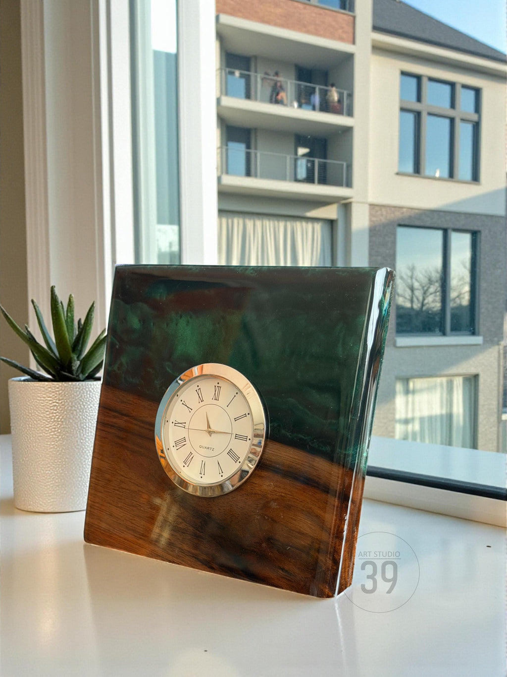 A rectangular wooden clock with a quartz movement. The clock face is white with black Roman numerals and a silver bezel. The top portion is a dark green resin. The base is a rich brown wood.