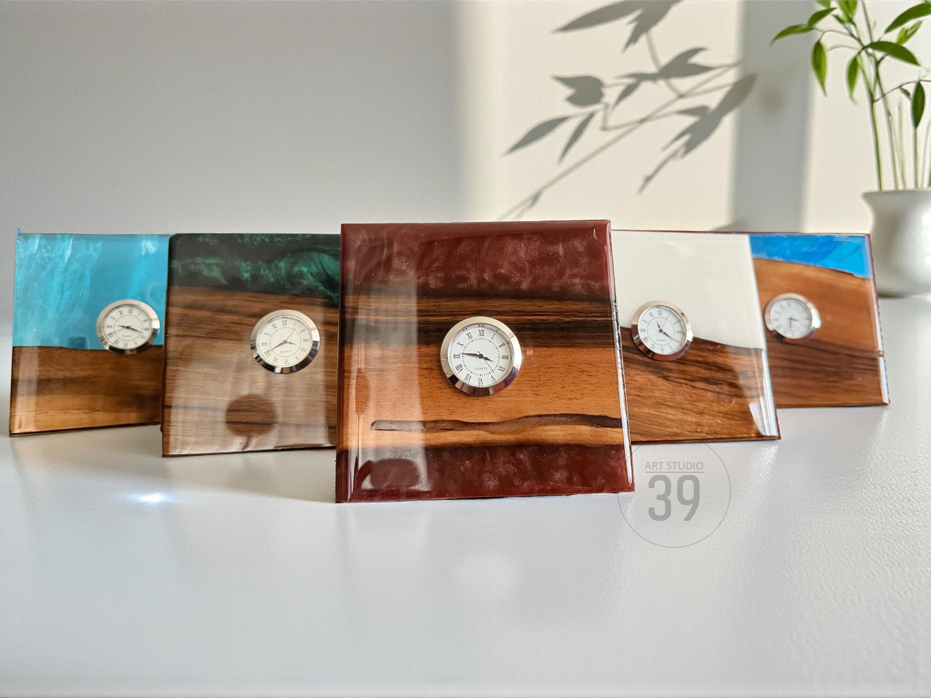 Five decorative wooden clocks with resin accents. Each clock features a small, round clock face with silver-colored trim. The resin colors include blue, green, white, and brown. The clocks are displayed on a white surface.