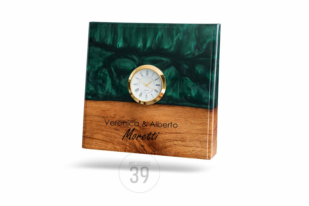 A rectangular wooden clock with a gold-rimmed clock face. The top half is a dark green, swirled resin, and the bottom half is wood. The clock face has Roman numerals. The names "Veronica &amp; Alberto Moretti" are engraved on the wood.