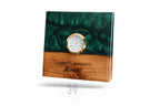 A rectangular wooden clock with a gold-rimmed clock face. The top half is a dark green, swirled resin, and the bottom half is wood. The clock face has Roman numerals. The names "Veronica &amp; Alberto Moretti" are engraved on the wood.