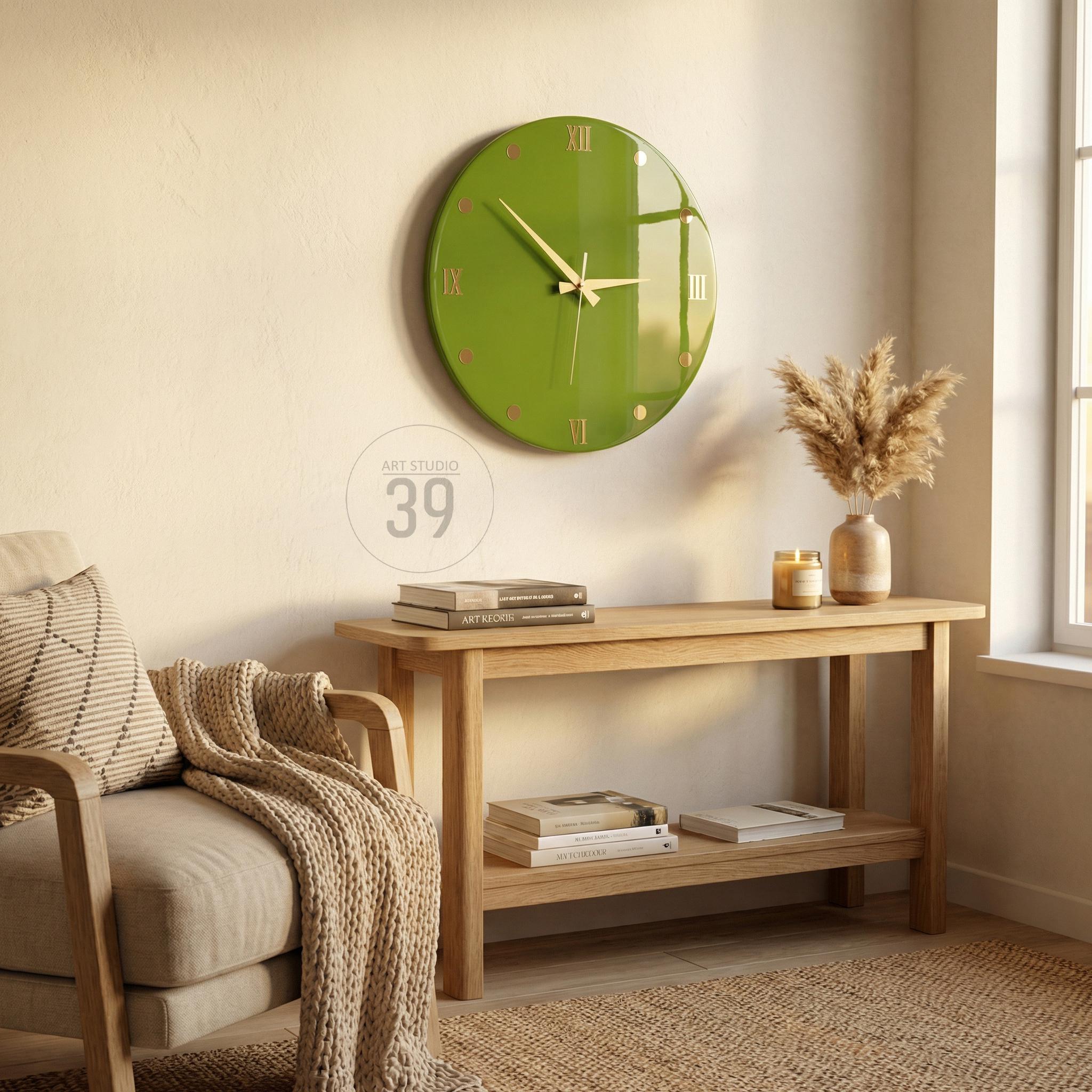 A green wall clock with gold hands and Roman numerals hangs above a wooden console table. The clock is round and has a glossy finish. The table holds books, a vase with dried flowers, and a lit candle. The text "ART STUDIO 39" is also visible.