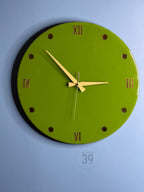 A round, lime green wall clock with gold-colored Roman numerals and hour markers. The clock hands are gold, and the clock face has a glossy finish. The text "ART STUDIO 39" is printed at the bottom. A decorative piece for any room.