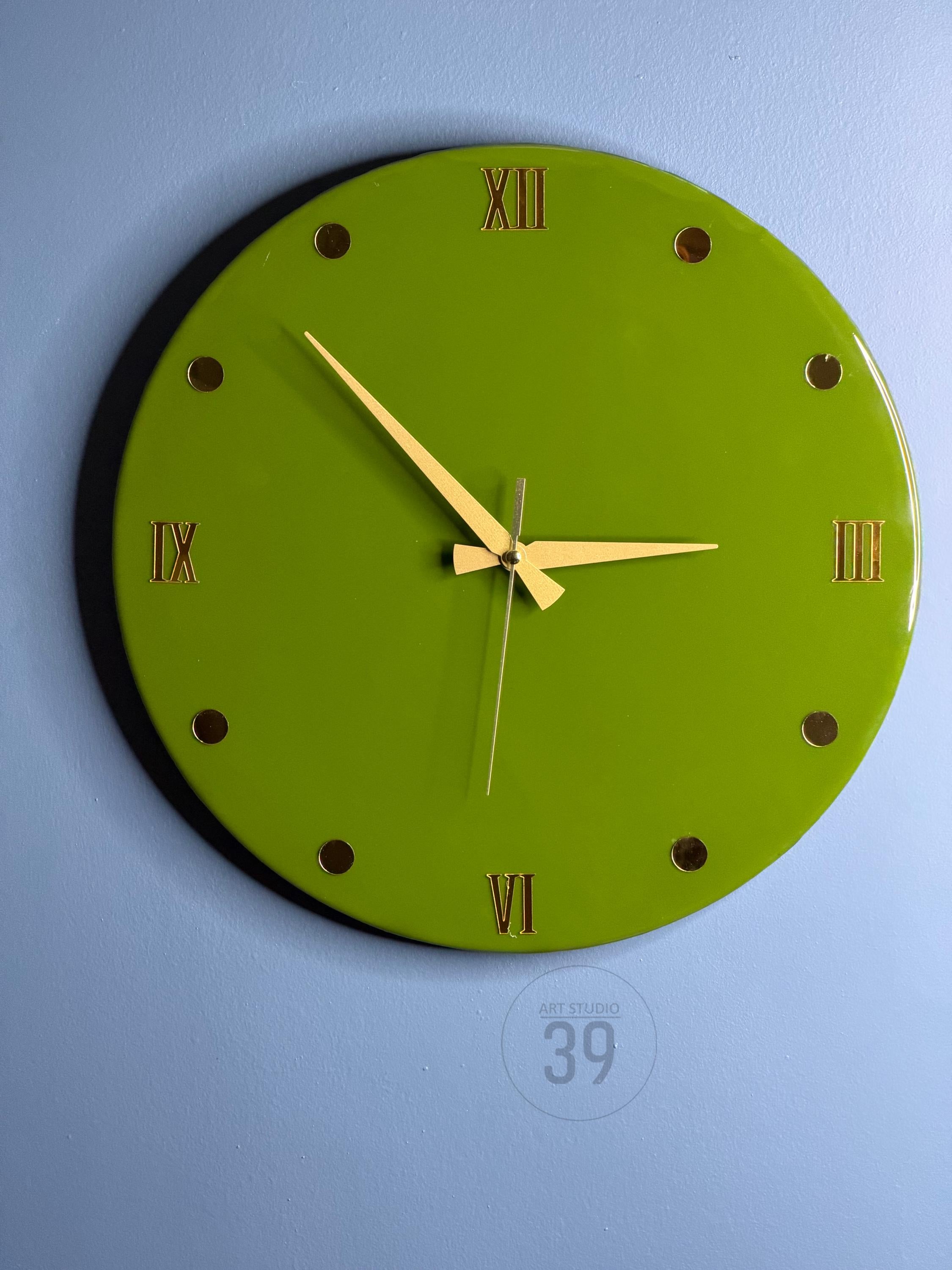 A round, lime green wall clock with gold-colored Roman numerals and hour markers. The clock hands are gold, and the clock face has a glossy finish. The text "ART STUDIO 39" is printed at the bottom. A decorative piece for any room.