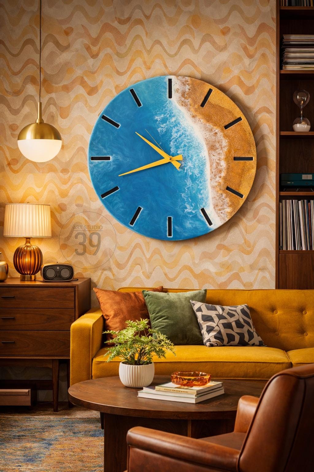 A round wall clock with a beach scene design. The clock face features a blue ocean, sandy shore, and yellow clock hands. Black markers indicate the hours. The clock is hanging on a patterned wall.
