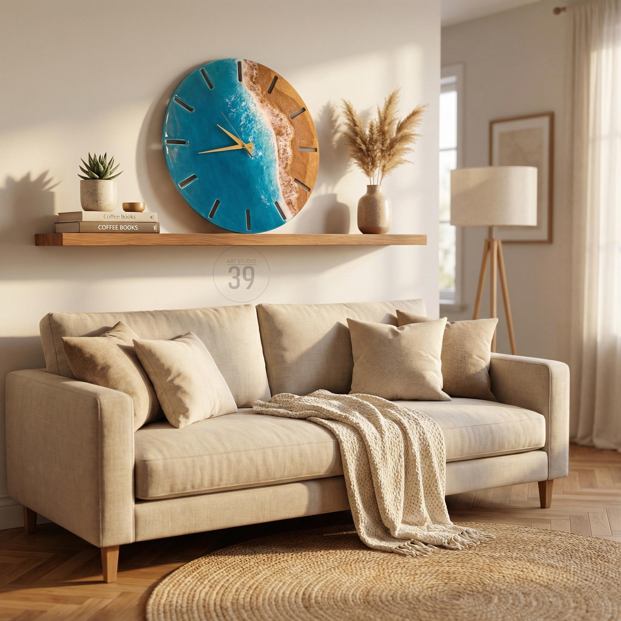 A large, round wall clock with a blue resin ocean design and gold-colored hands. The clock is mounted on a white wall above a beige sofa with throw pillows and a blanket. A wooden shelf holds books and a potted plant.