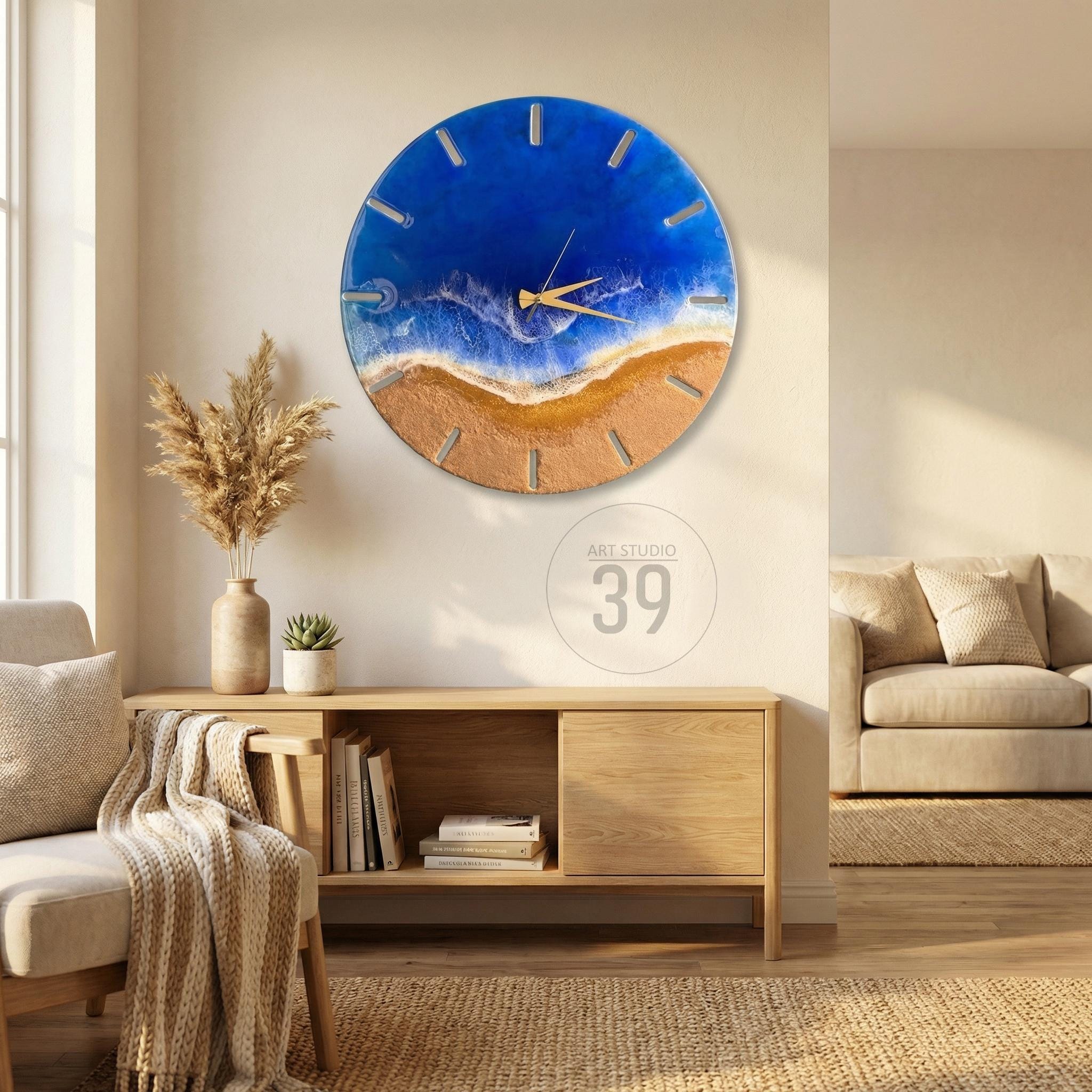 A round wall clock with a beach scene design. The clock face features a blue ocean, a sandy beach, and gold-colored clock hands. The clock is mounted on a white wall. The text "ART STUDIO 39" is in the lower center.