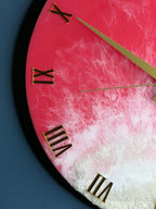 A close-up of a round wall clock with a pink and white marbled design. The clock features gold-colored Roman numerals and hands. The clock's face has a textured, ocean-like appearance.