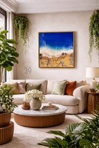 A living room scene featuring a large abstract painting of a beach with blue water and golden sand. A cream-colored sofa is adorned with decorative pillows. A round coffee table and potted plants complete the decor.