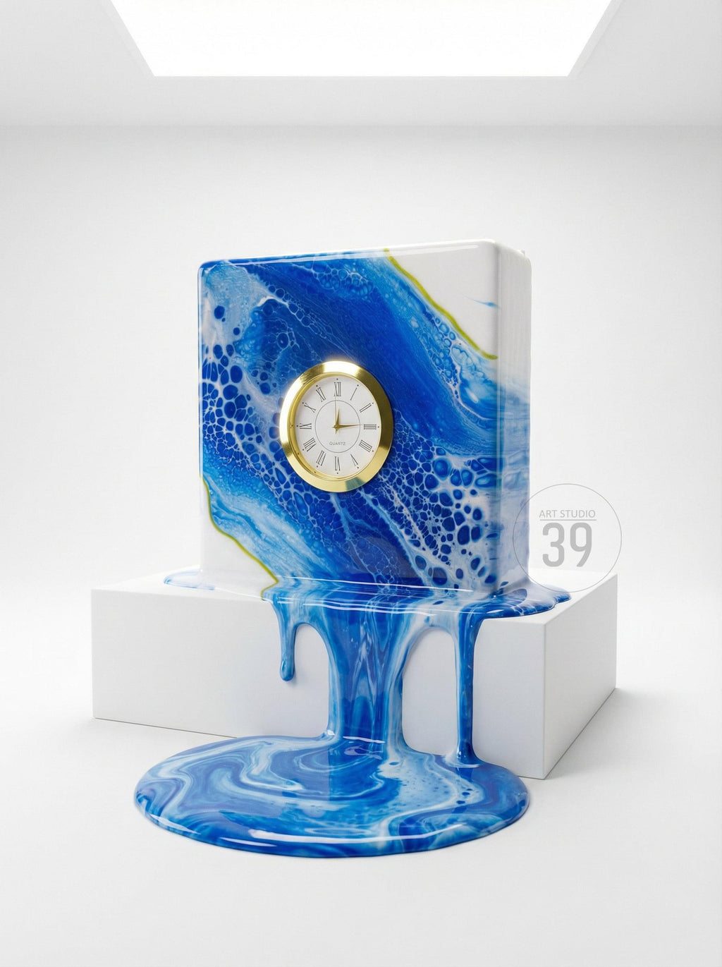 A unique, abstract clock design. The square clock features a gold-colored clock face with Roman numerals. The clock's surface is a blend of blue and white, with a dripping effect. The base is white, and the text "ART STUDIO 39" is visible.