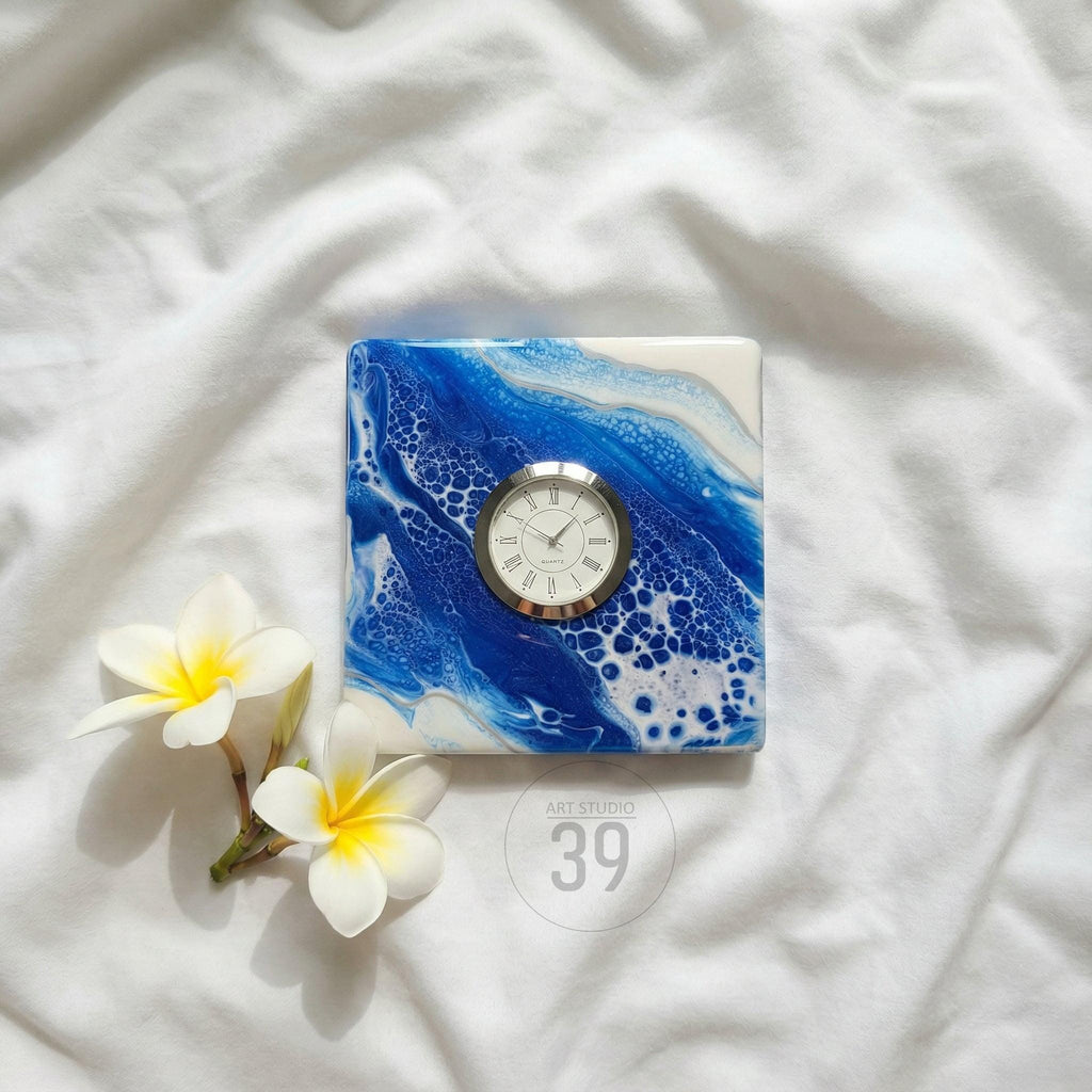Square clock with a white face and silver bezel set into a blue and white abstract design. The clock face has black Roman numerals. The words "ART STUDIO 39" are printed on the bottom right.