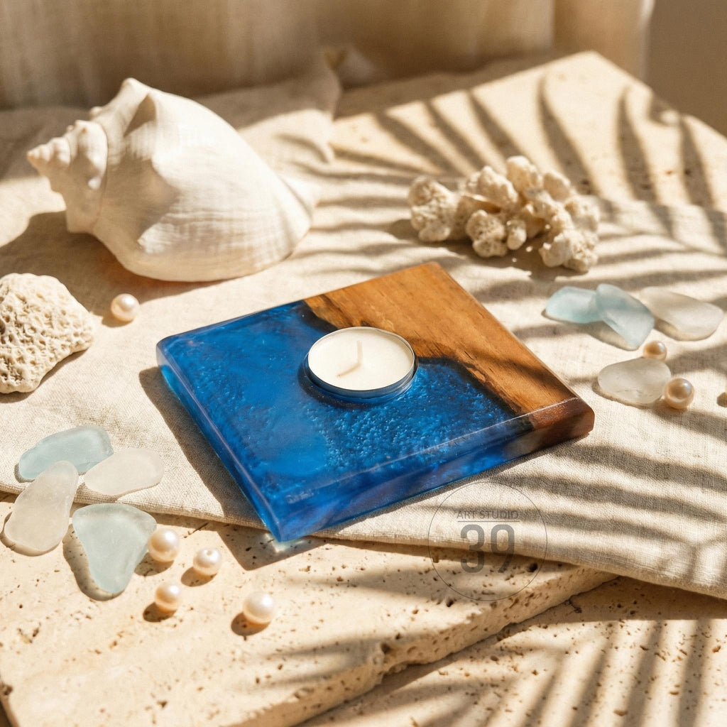 A square candle holder with a wooden top and a blue resin base. A small white candle sits in the center. The image also includes a seashell, pearls, and sea glass, suggesting a coastal theme.