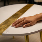 A white round table with a gold stripe down the center. The table has gold legs and a hand with several gold rings on it. The table has the text "ART STUDIO 39" on the side.