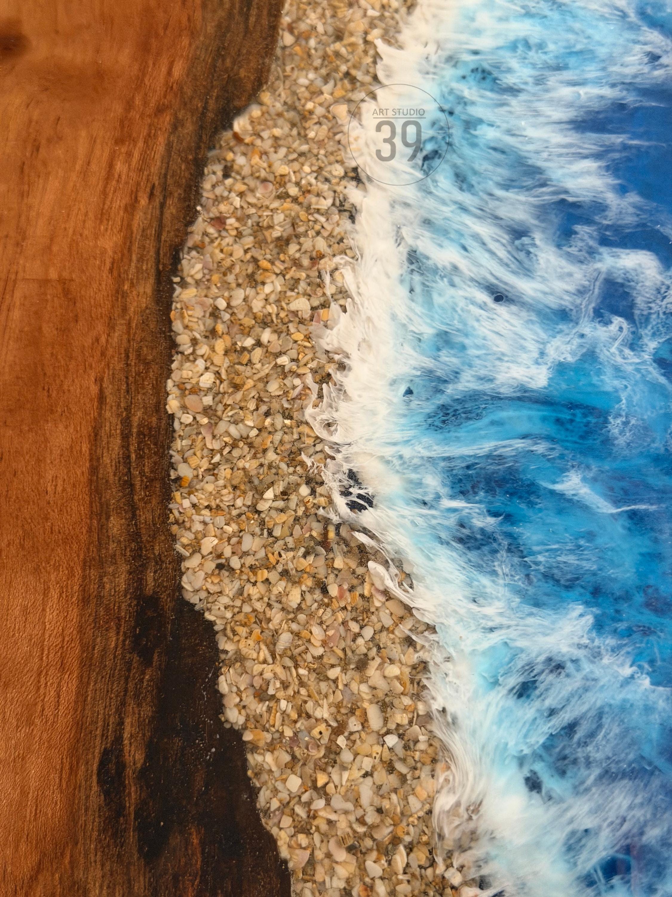 Close-up of a wooden surface with a beach scene. The design features a sandy shore made of small pebbles, with foamy white waves and blue water. The text "ART STUDIO 39" is visible.