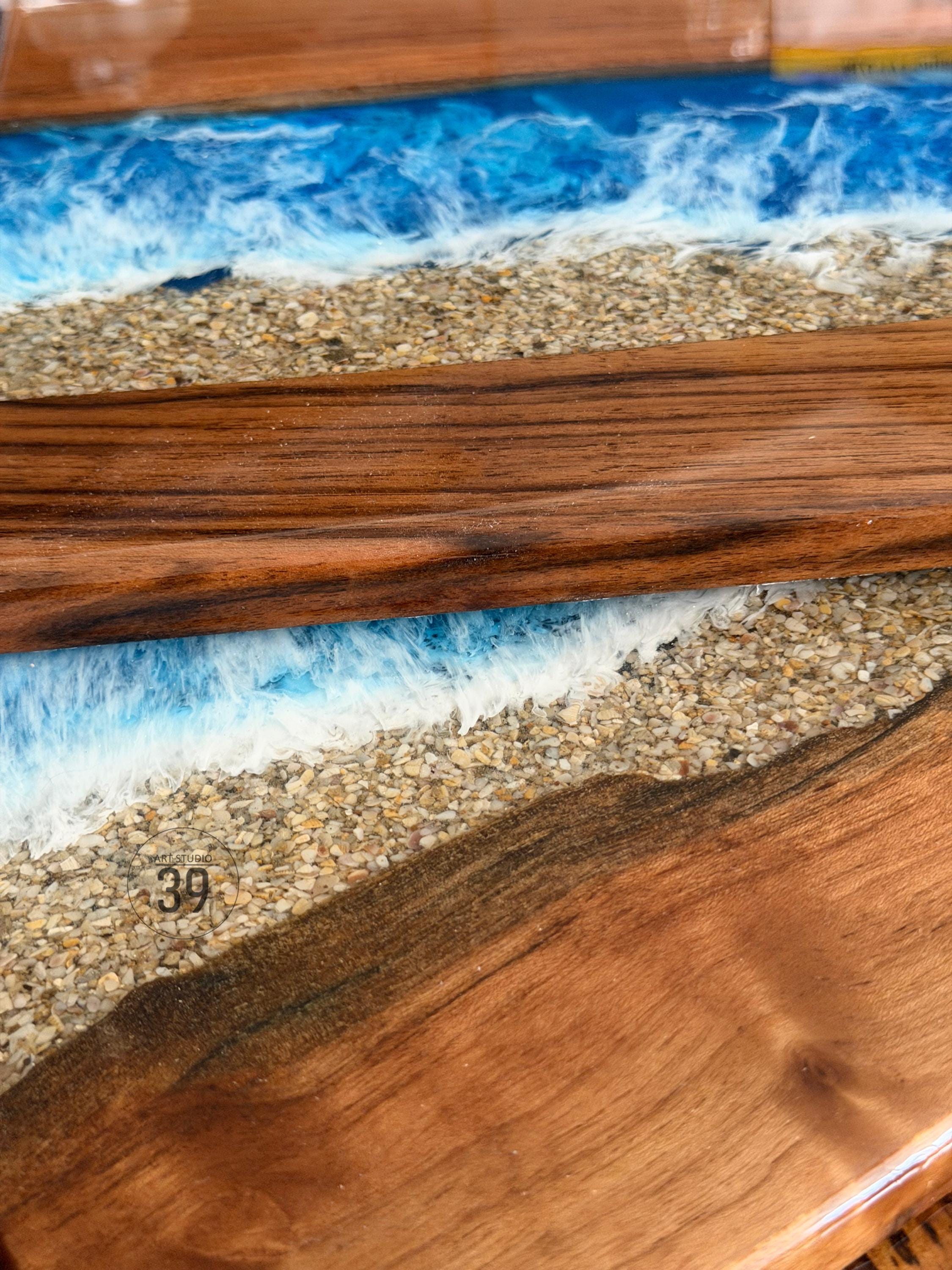 Close-up of a wooden art piece with a beach scene. The design incorporates layers of wood, sand, and resin to depict ocean waves. The number "39" is visible on the surface.