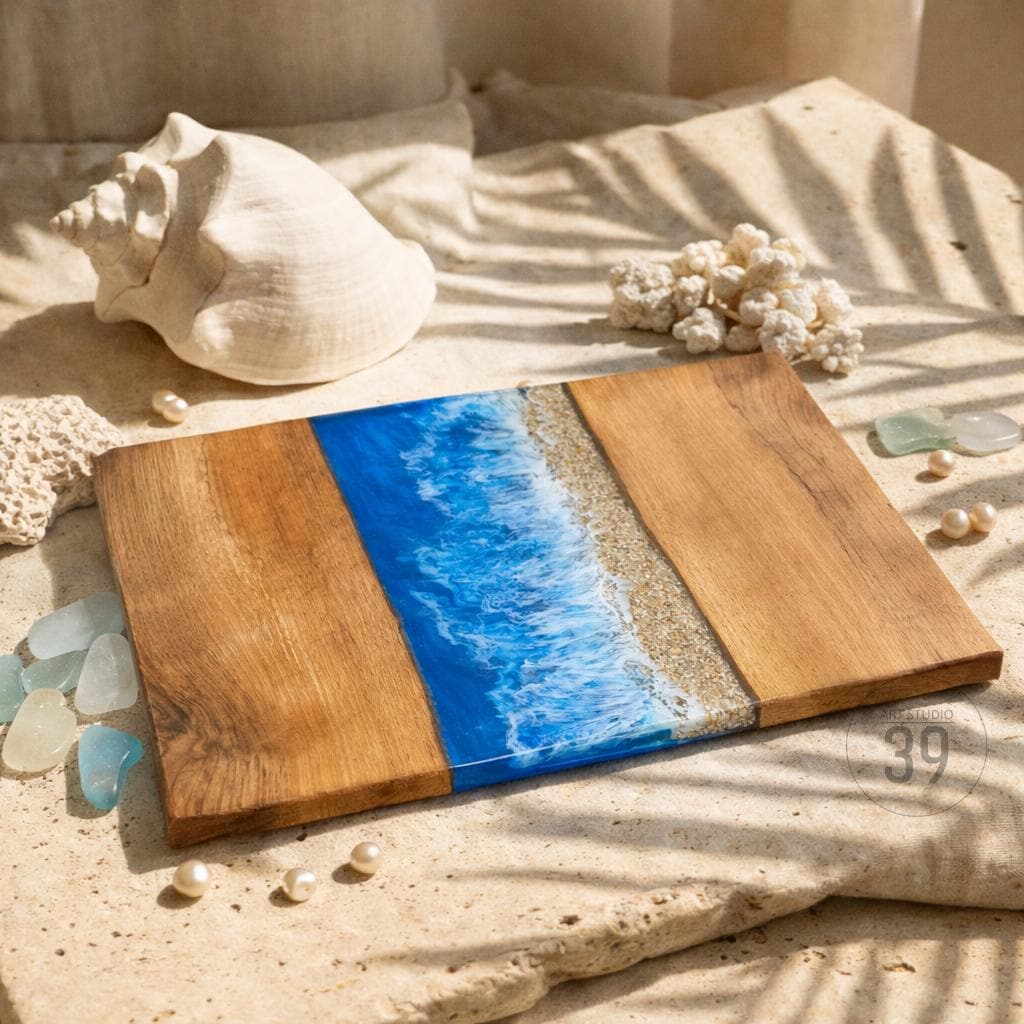 A rectangular wooden serving board with a blue resin ocean design and a sandy beach strip. The board has a natural wood grain finish and is decorated with seashells and pearls.