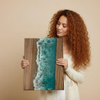 Wooden wall art featuring a beach scene with a turquoise ocean and sandy shore. The artwork is framed with dark wood and has a resin ocean effect. The piece is rectangular and evokes a coastal theme.
