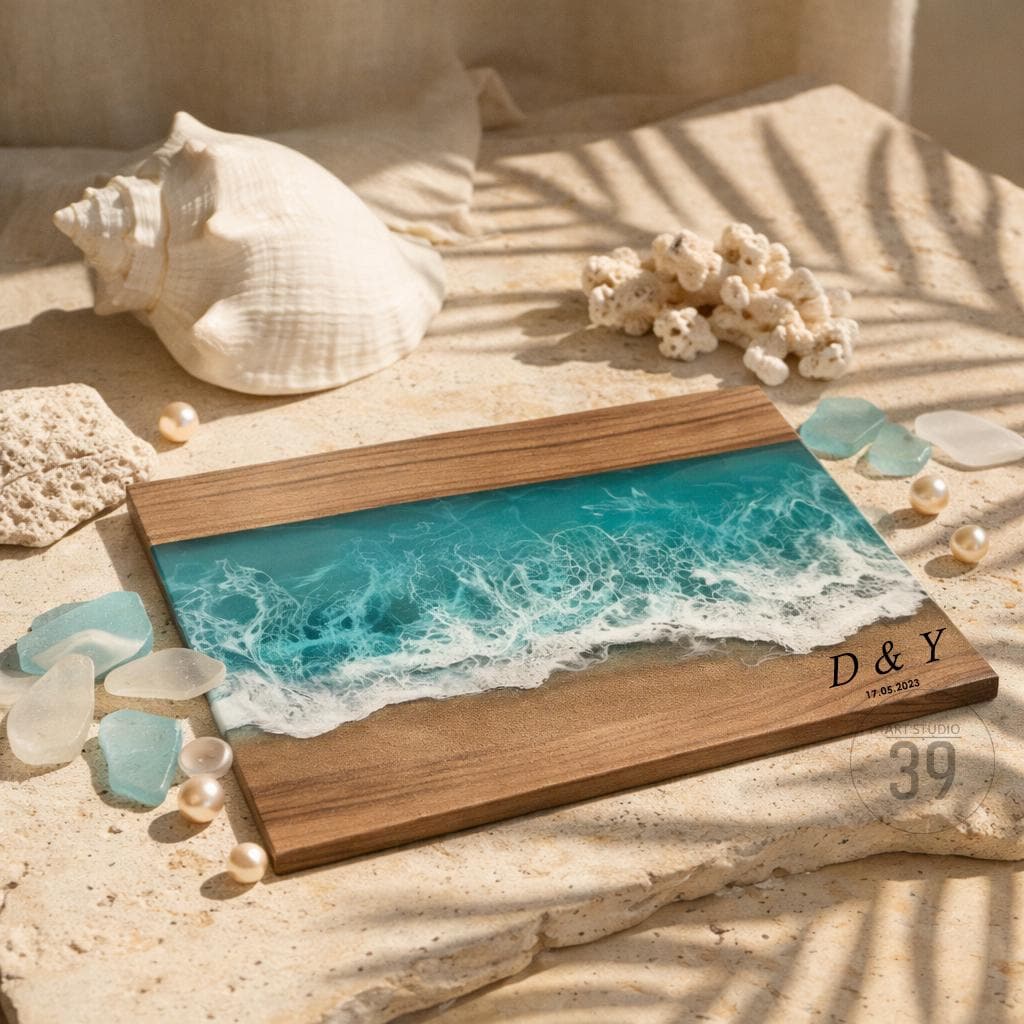 Wooden serving board with a resin ocean design. The board features a turquoise and white wave pattern, with a sandy beach effect. The initials "D &amp; Y" and the date "17.05.2023" are engraved on the board. The board is surrounded by seashells and pearls.