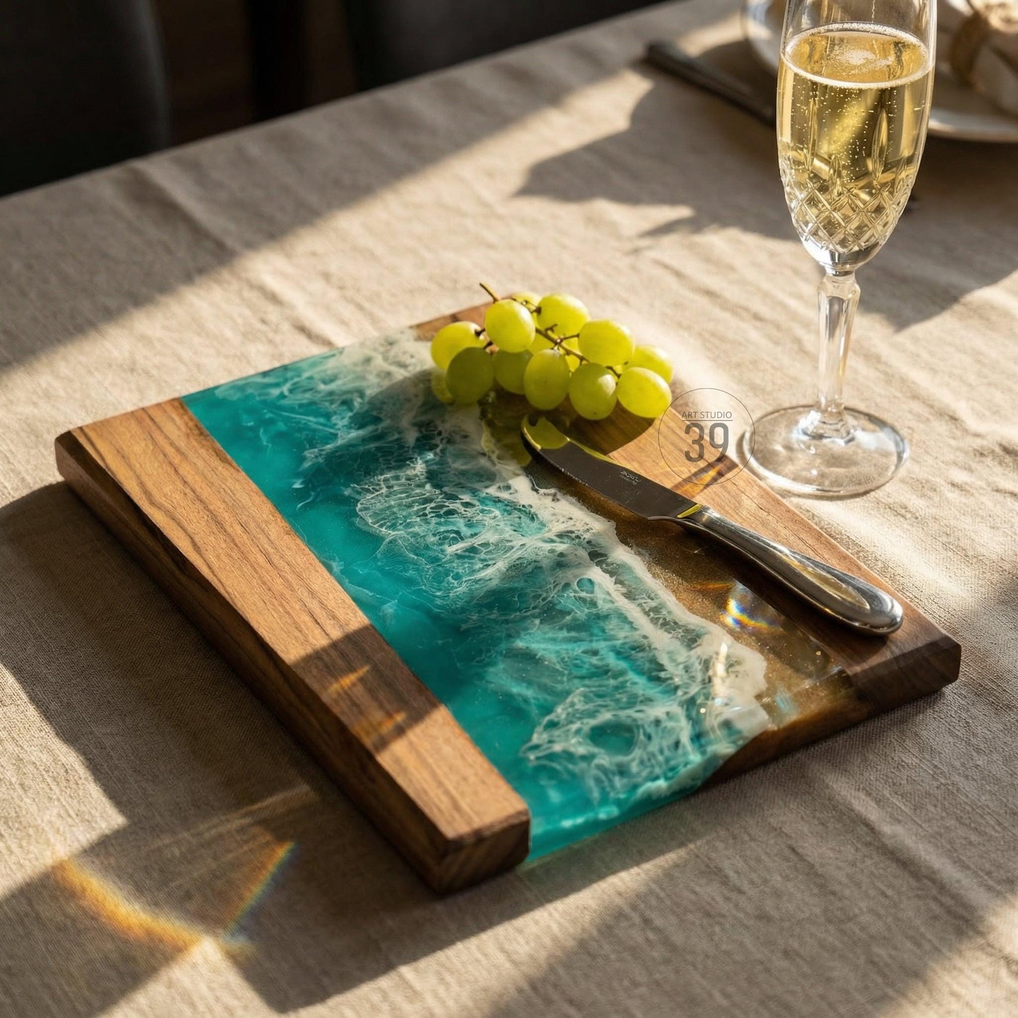 Wooden serving board with a turquoise resin design resembling ocean waves. The board has a natural wood border and a stainless steel knife. A bunch of green grapes rests on the board.