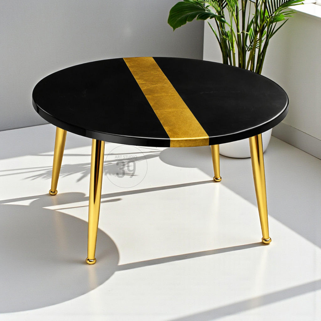 A round black coffee table with a gold stripe down the center. The table has gold-colored metal legs. The table is approximately 30 inches in diameter.