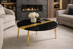 A round black coffee table with a gold stripe and gold legs. The table has a vase of white flowers, a book, and a decorative object on top. The table is 39 inches in diameter.