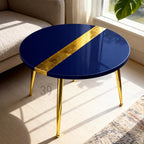 A round, navy blue coffee table with a gold leaf stripe across the top. The table has gold-colored metal legs. The text "ART STUDIO 39" is visible on one of the legs. The table is in a living room setting.
