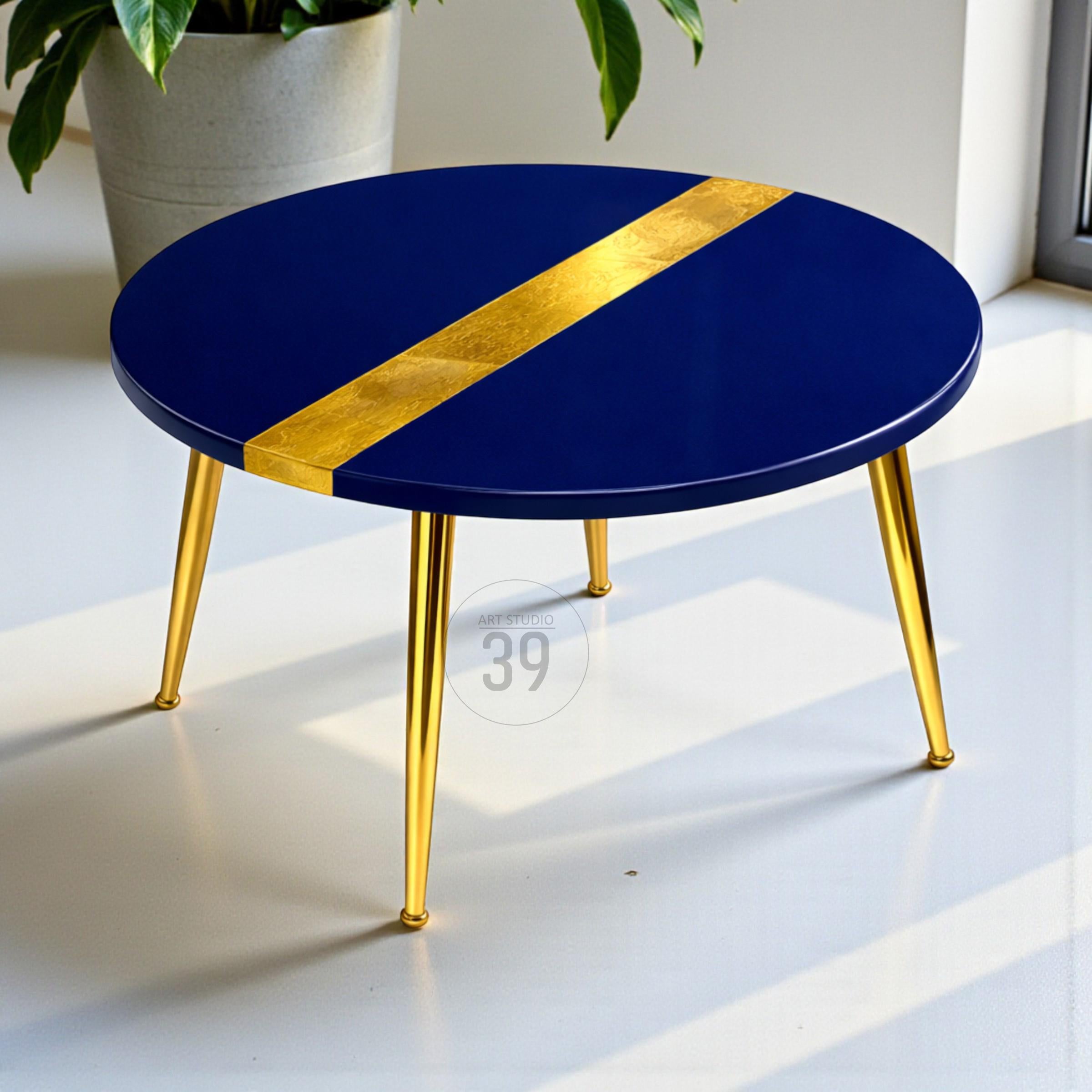 A round, navy blue coffee table with a gold stripe across the top. The table has gold, tapered legs. The table is approximately 18 inches in diameter.