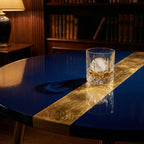 A round, navy blue table with a gold stripe and gold legs. A rocks glass with a large ice sphere and amber liquid sits on the table. The number "39" is visible on the gold stripe.