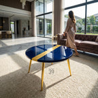 A round, navy blue coffee table with a gold stripe down the center. The table has gold-colored legs and is set on a cream-colored rug. The number "39" is printed on the table.