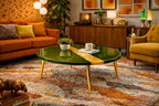 A retro-style living room with a green and gold coffee table with gold legs. The table is in front of an orange sofa with decorative pillows. A patterned rug and vintage decor complete the scene.
