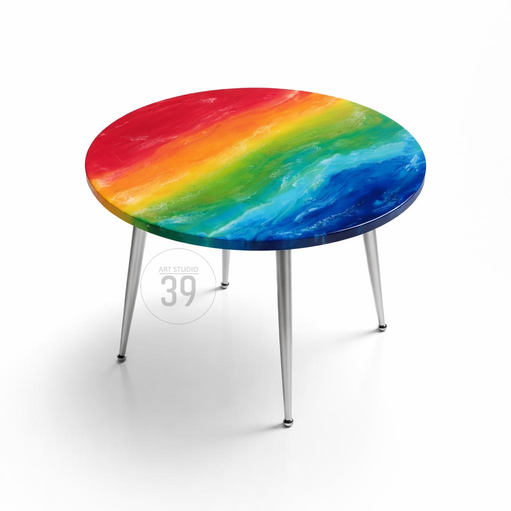 A round coffee table with a rainbow-colored top and silver legs. The tabletop features a vibrant blend of red, orange, yellow, green, and blue hues. The table has four slender, silver legs. The text "39" is visible.