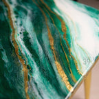 Close-up of a table surface with a vibrant green and white marbled design, accented by gold metallic streaks. The table has a glossy finish and a modern aesthetic. The corner of the table shows the text "ART STUDIO 39".
