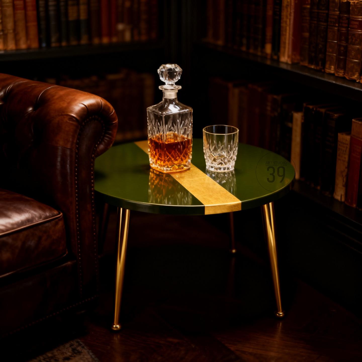A green and gold accent table with a crystal decanter and a rocks glass. The table has gold legs and a gold stripe down the center. The decanter is filled with amber liquid.