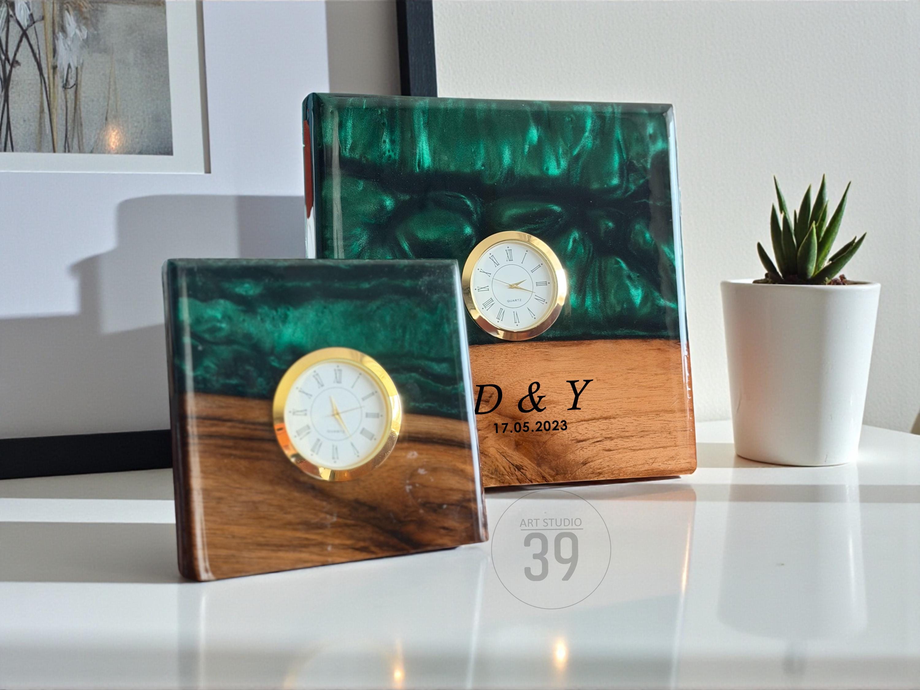 Two square clocks with gold-colored clock faces. The top portion of each clock is a deep green, marbled resin, while the bottom is a warm wood tone. One clock has the initials "D &amp; Y" and the date "17.05.2023".