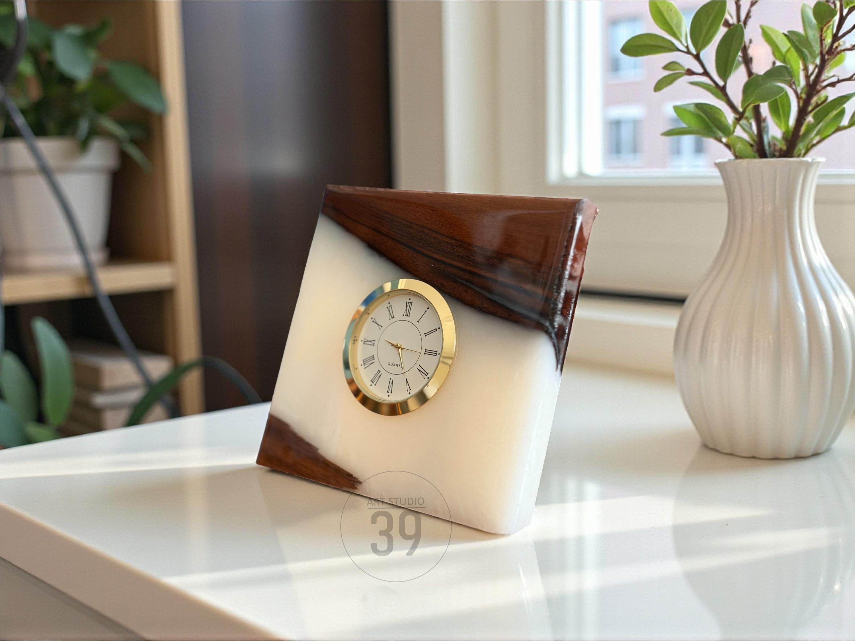 A square wooden clock with a gold-colored clock face. The clock is made of wood and white resin, with a glossy finish. The clock is on a white surface.