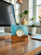 A square desk clock with a gold-colored bezel and white clock face. The clock is set into a block of wood and blue resin. The base of the clock is wood, and the top is blue resin. The text "ART STUDIO 39" is visible.