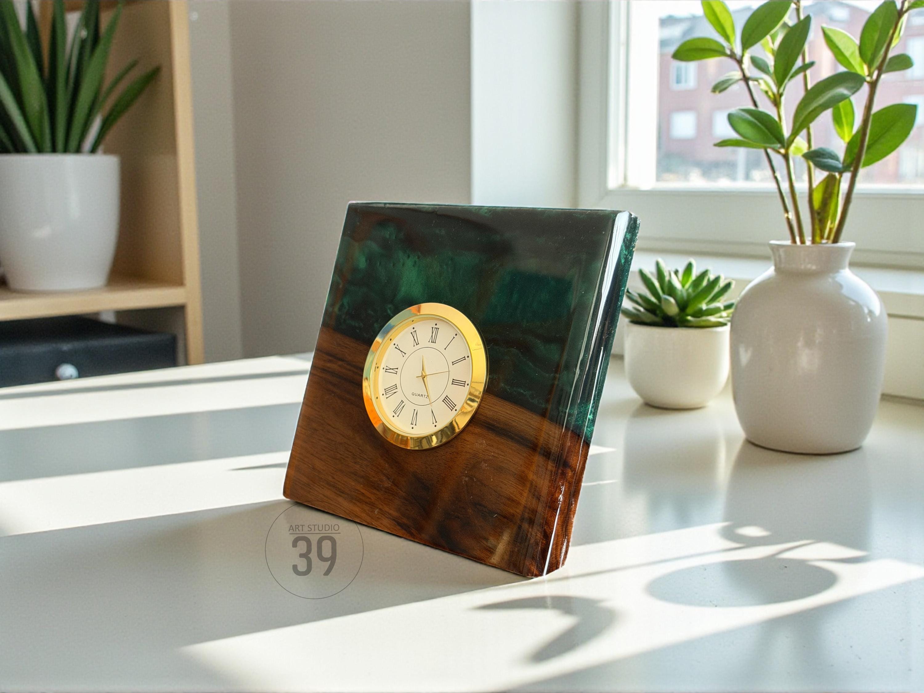 A square wooden clock with a gold-colored clock face. The clock is made of wood and resin, with a dark green and brown color scheme. The clock is on a white surface.