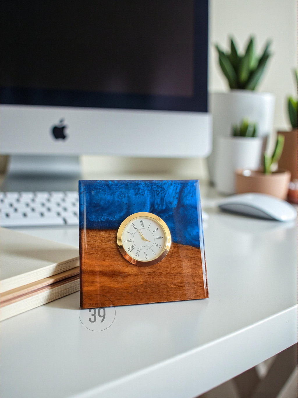 A square desk clock with a gold-colored bezel and a white clock face. The clock is set into a wooden base with a blue resin top. The number "39" is printed on the bottom of the clock.